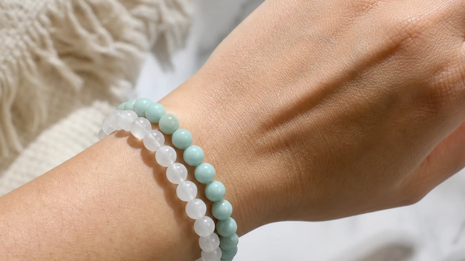 Amazonite and Selenite crystal bracelets worn together stacked on one wrist, real hand, natural daylight, minimalist wellness lifestyle scene