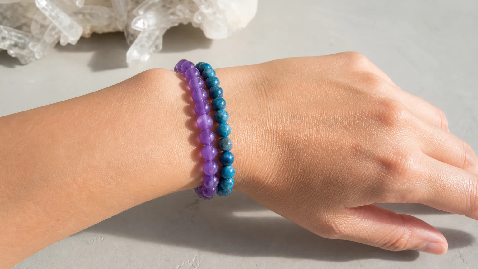 Amethyst and Apatite crystal bracelets worn together stacked on one wrist, real hand, natural daylight, minimalist wellness lifestyle scene