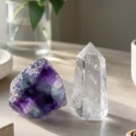 A single fluorite crystal and a clear quartz point resting on a clean desk beside a lit candle, soft directional light, uncluttered calm workspace