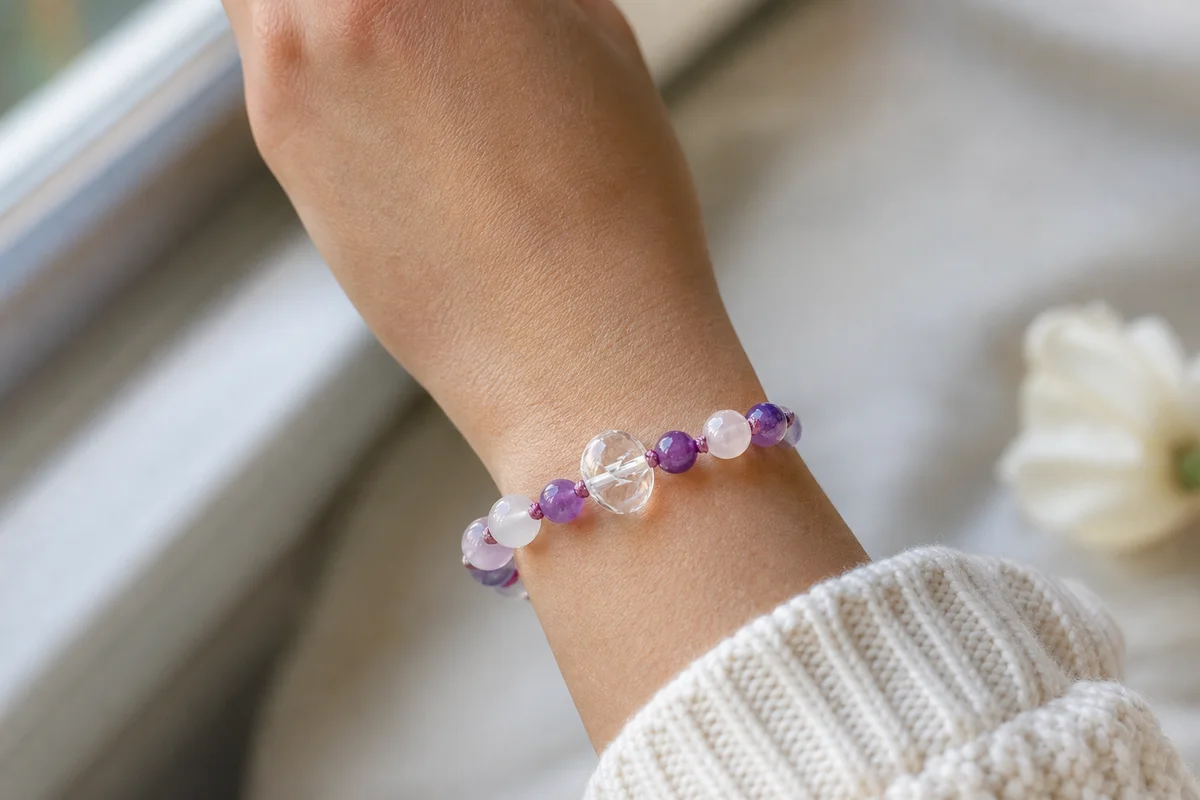 A programmed crystal bracelet worn as a daily reminder — a gemstone bracelet on a wrist in soft natural light, clean and minimal composition, realistic jewelry photography showing the cord and stones as a personal keepsake, no text