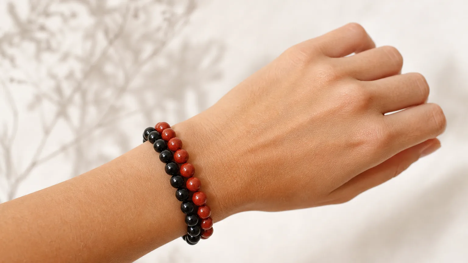 Obsidian and Red Jasper crystal bracelets worn together stacked on one wrist, real hand, natural daylight, minimalist wellness lifestyle scene
