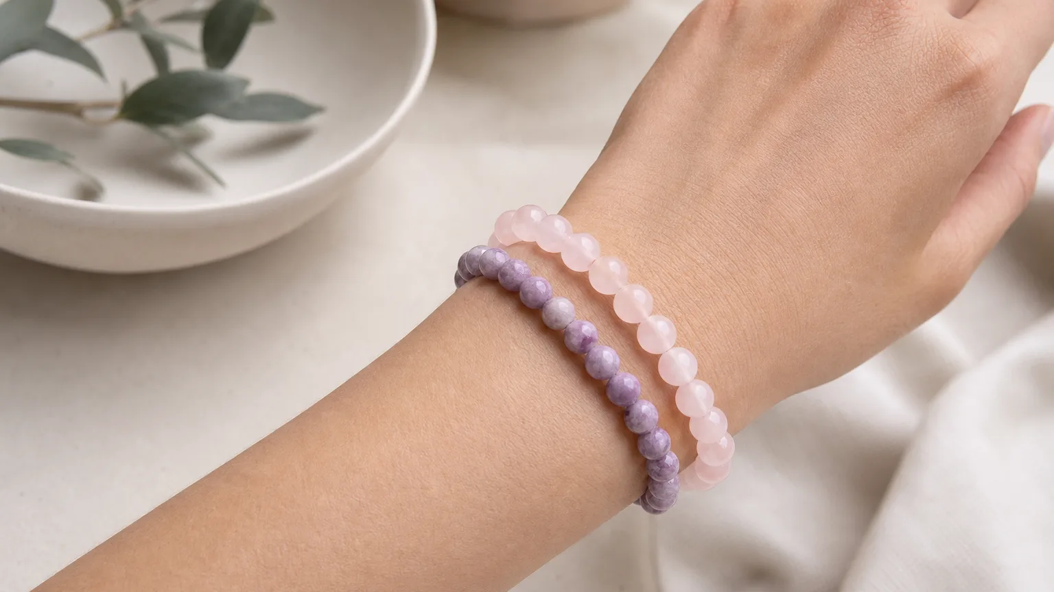 Rose Quartz and Lepidolite crystal bracelets worn together stacked on one wrist, real hand, natural daylight, minimalist wellness lifestyle scene