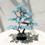 May include: A blue aquamarine crystal bonsai tree with copper wire branches. The tree is in a small black pot with a textured surface.
