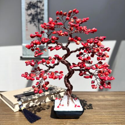 May include: A red coral wire wrapped bonsai tree in a black pot. The tree is made of copper wire and red coral beads. The tree is sitting on a wooden table.