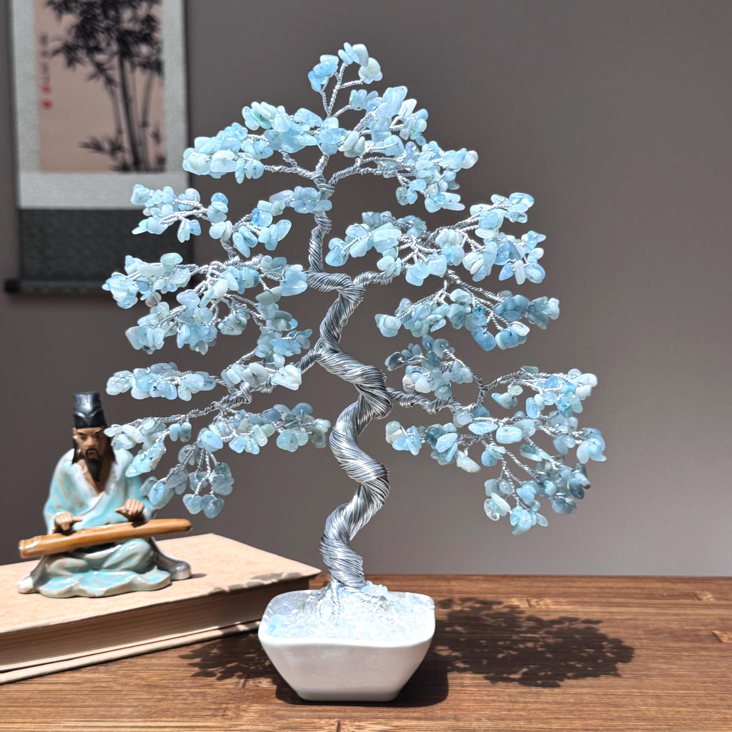 Natural Aquamarine Bonsai Tree - Image 1 May include: A wire-wrapped crystal tree with blue aquamarine stones. The tree is in a white ceramic pot and is on a wooden table.