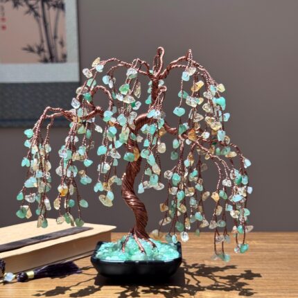 May include: A decorative copper wire tree sculpture with cascading branches adorned with green and yellow gemstone chips. The tree sits in a black pot filled with green stones, creating a unique and artistic display.