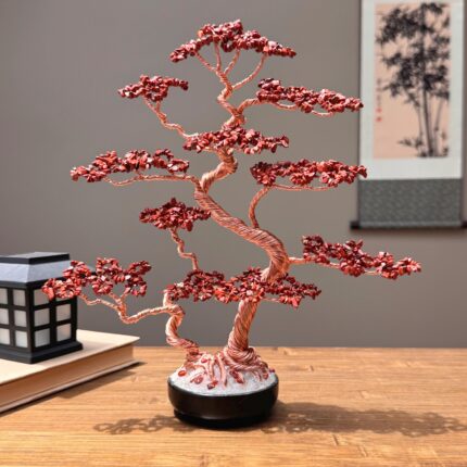 May include: A decorative bonsai tree sculpture crafted from twisted copper-colored wire and small, faceted red stone chips. The tree features multiple layered branches extending from a central trunk, anchored in a round black base with white gravel.