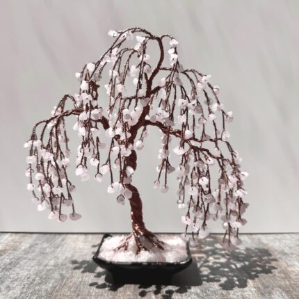 May include: A weeping willow tree made of copper wire and pink quartz crystals. The tree is in a black pot with white quartz crystals.