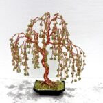 May include: A copper wire sculpture of a weeping willow tree with green gemstone leaves. The tree is in a black pot with a green gemstone base.