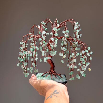 May include: A decorative wire tree sculpture featuring a twisted copper-colored metal trunk and branches adorned with numerous small, light green tumbled gemstone chips that hang down to resemble the foliage of a weeping willow tree.