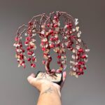 May include: A handcrafted copper wire bonsai tree sculpture. The tree features a twisted copper trunk, cascading branches, and red, yellow, and clear gemstone "leaves." The tree is planted in a small black square pot.