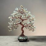 May include: A decorative tree sculpture featuring a twisted copper wire trunk and branches adorned with numerous small, pale green, translucent stone chips. The tree is anchored in a square black base filled with matching green stone fragments.
